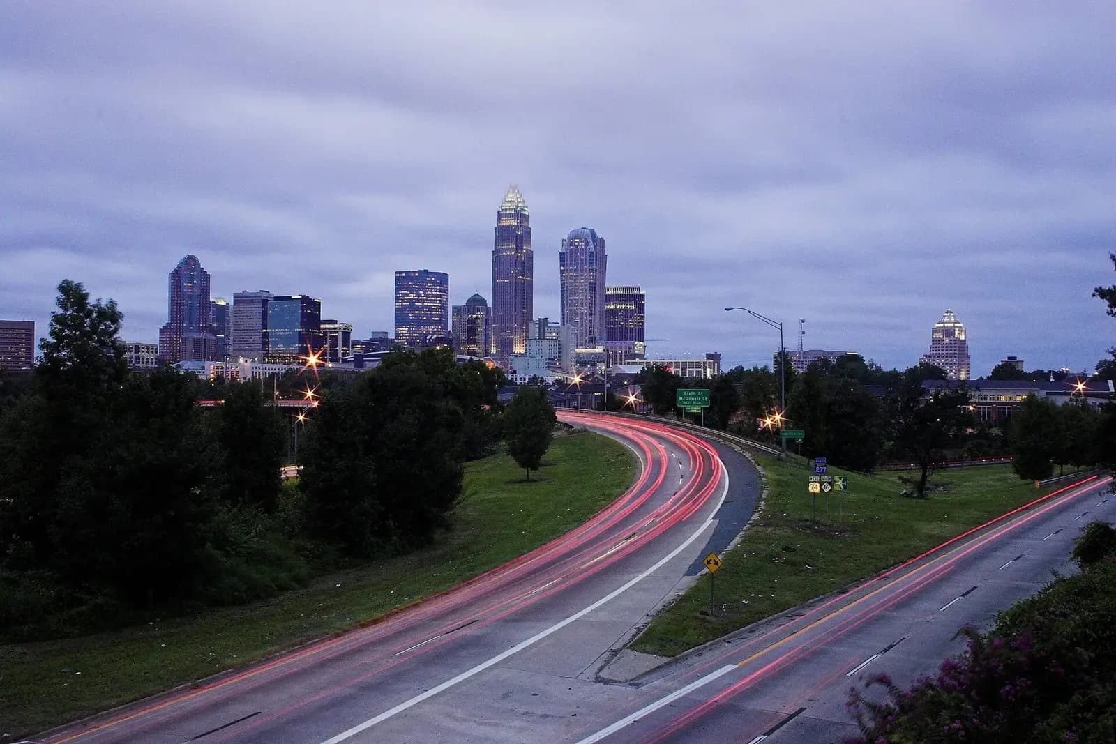 Charlotte skyline under storm clouds with traffic light trails on a curving road